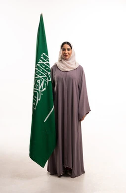 امرأة سعودية بالعباية تقف بجانب علم السعودية