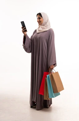 امرأة سعودية تحمل حقائب تسوق وهاتف ذكي