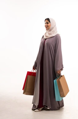 امرأة سعودية بالعباءة تحمل حقائب تسوق على خلفية بيضاء