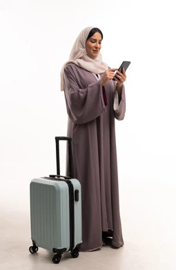 امرأة إماراتية مع حقيبة سفر تستخدم الهاتف الذكي