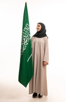 امرأة سعودية بالعباءة تقف بجانب علم السعودية في الاستوديو