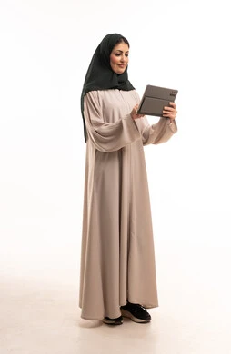 امرأة سعودية بعباءة تستخدم جهاز لوحي خلفية بيضاء