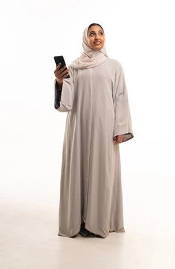 امرأة سعودية بعباءة تستخدم الهاتف الذكي بخلفية بيضاء