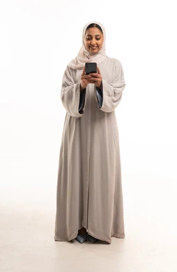 امرأة إماراتية بعباءة رمادية تستخدم الهاتف الذكي امرأة إماراتية بعباءة رمادية تستخدم الهاتف الذكي