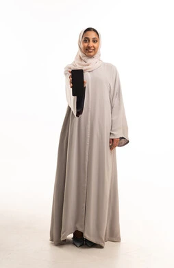 امرأة سعودية تحمل هاتف ذكي بعباءة رمادية في الاستوديو