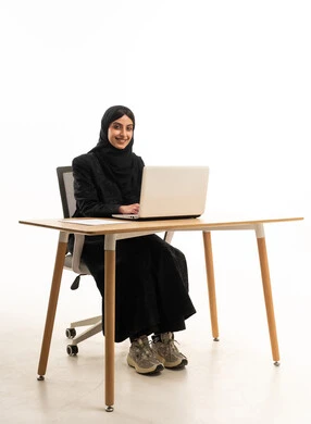امرأة سعودية تعمل على جهاز لابتوب خلف مكتب عمل