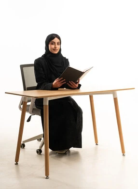 امرأة إماراتية تقرأ كتاباً خلف مكتب عمل عصري