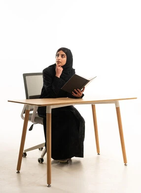 امرأة سعودية بالعباءة تقرأ على مكتب العمل خلفية بيضاء