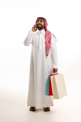 رجل سعودي يحمل حقائب تسوق ويتحدث بالهاتف