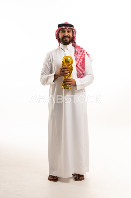 رجل سعودي بالزي التقليدي يحمل كأس البطولة الذهبي في الاستوديو