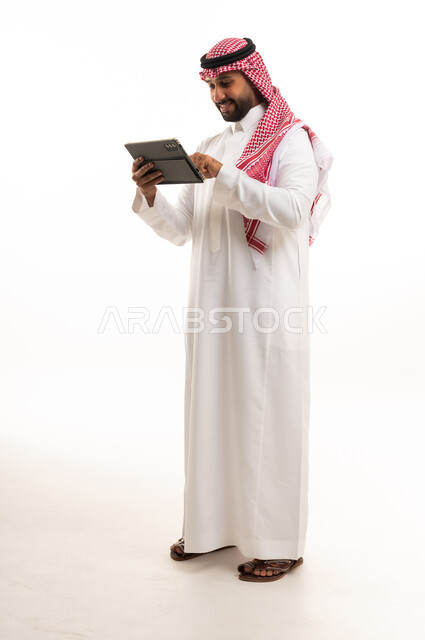 رجل سعودي بالزي التقليدي يستخدم جهاز لوحي رقمي