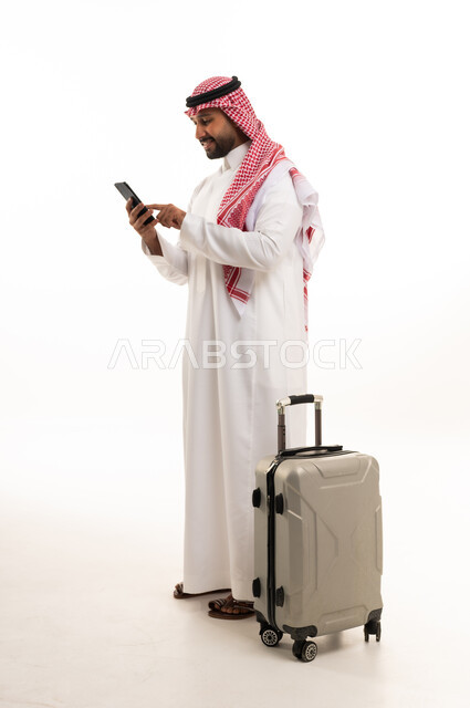 رجل سعودي مع حقيبة سفر يستخدم الهاتف الذكي