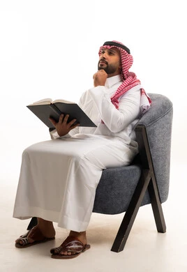 رجل سعودي بالزي التقليدي يقرأ كتاباً في الاستوديو