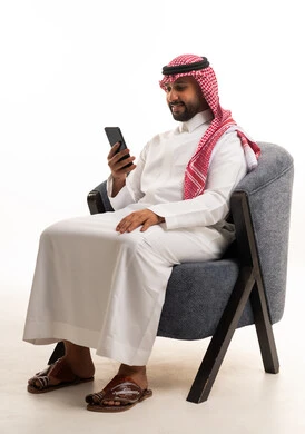 A Saudi man in traditional attire using a smartphone.