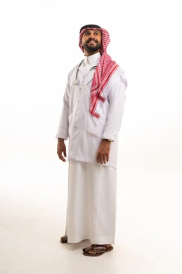 A Saudi doctor in traditional attire and a white medical coat.