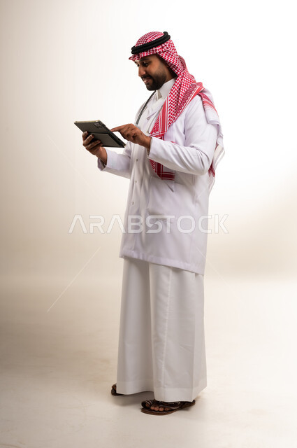 طبيب سعودي يرتدي المعطف الطبي ويستخدم جهاز تابلت رقمي