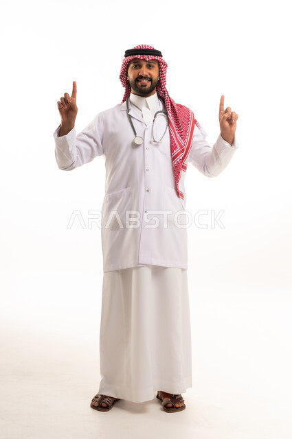 طبيب سعودي يرتدي المعطف الطبي ويشير للأعلى خلفية بيضاء