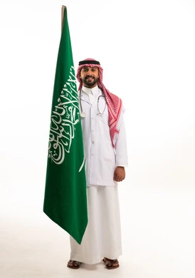 طبيب سعودي يحمل العلم الوطني بزي المستشفى الرسمي