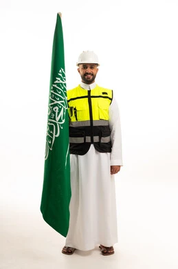 A Saudi man holding the national flag in traditional dress and a protective vest.