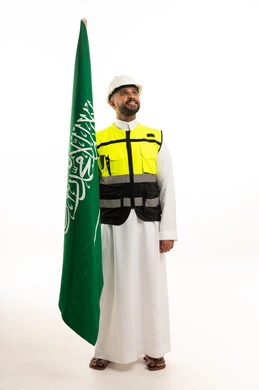 A Saudi man holding the national flag in traditional dress and a protective vest.