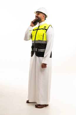 A Saudi engineer wearing a safety vest and using a mobile phone.