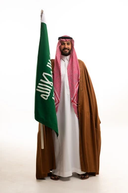 رجل سعودي يحمل علم المملكة العربية السعودية بالبشت التقليدي