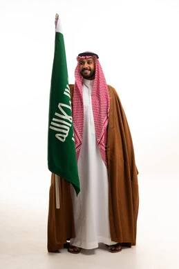 رجل سعودي بالبشت والزي التقليدي يحمل العلم