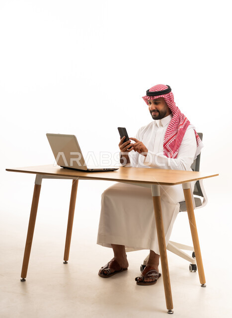 Saudi Man in Traditional Attire Using Smartphone at Desk