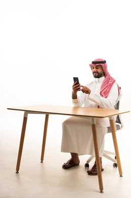 Saudi Man Using Smartphone at Desk on White Background