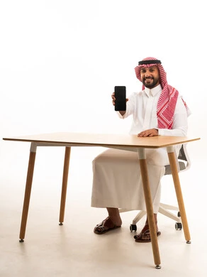 Saudi Man in Thobe Holding Smartphone at Desk