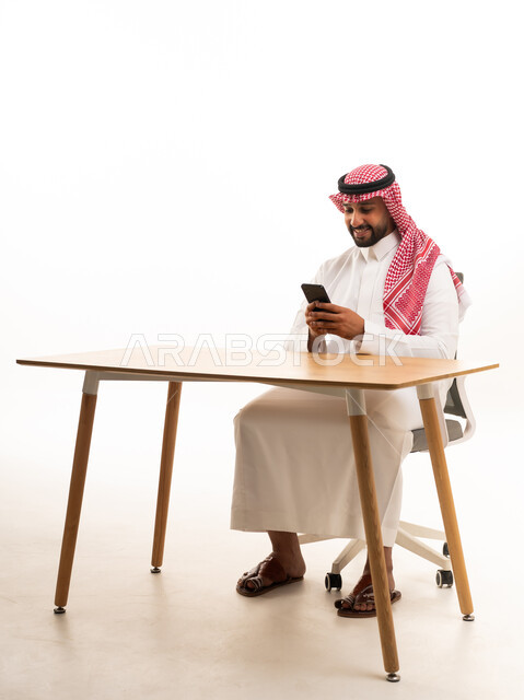 رجل سعودي يستخدم الهاتف الذكي خلف مكتب في استوديو