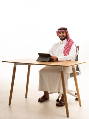 Saudi Man in Traditional Dress Using Tablet at Desk
