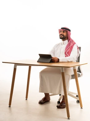 Saudi Man in Traditional Dress Using Tablet at Desk