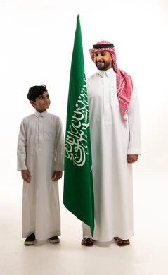 رجل سعودي وطفل مع العلم الوطني على خلفية بيضاء