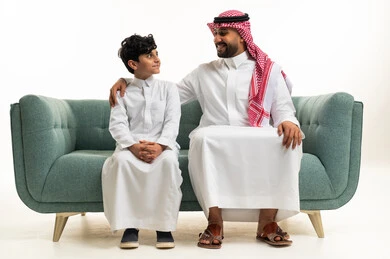 أب سعودي وابنه باللباس التقليدي على الأريكة