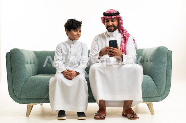Saudi Man and Boy Using Smartphone on Green Sofa Indoors