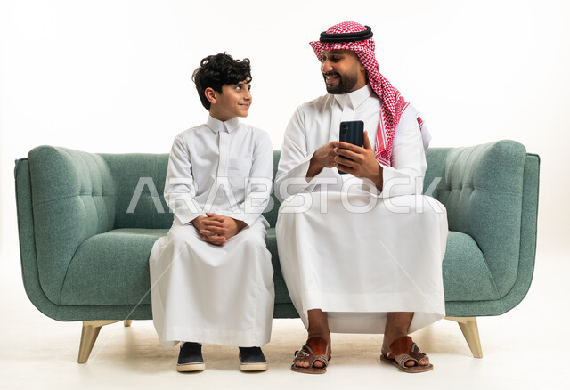 أب سعودي وابنه يستخدمان الهاتف الذكي على الأريكة