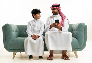 أب سعودي وابنه يستخدمان الهاتف الذكي على الأريكة