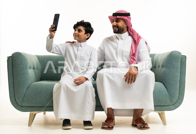 رجل وطفل سعوديان يستخدمان الهاتف على الأريكة