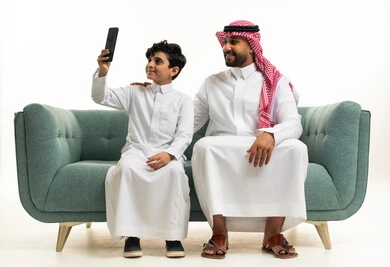 رجل وطفل سعوديان يستخدمان الهاتف على الأريكة