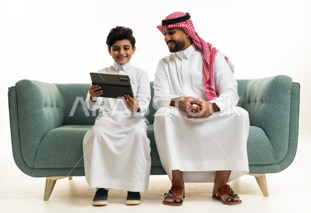 أب سعودي وطفله يستخدمان الجهاز اللوحي على الأريكة