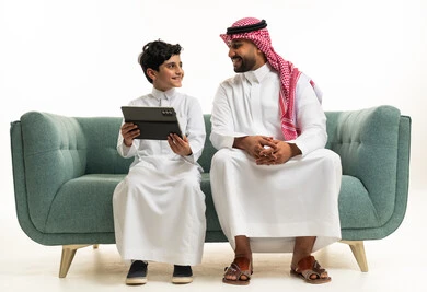 رجل سعودي وطفل يستخدمان جهاز لوحي على الأريكة