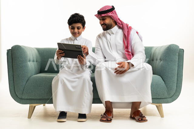 رجل سعودي وطفل يستخدمان الجهاز اللوحي على أريكة خضراء