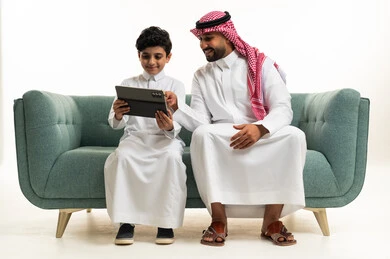 Saudi Man and Boy Using Tablet on Green Sofa in Thobe