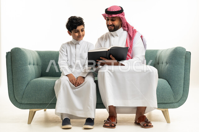 رجل سعودي وطفل يقرآن كتاباً على أريكة خضراء