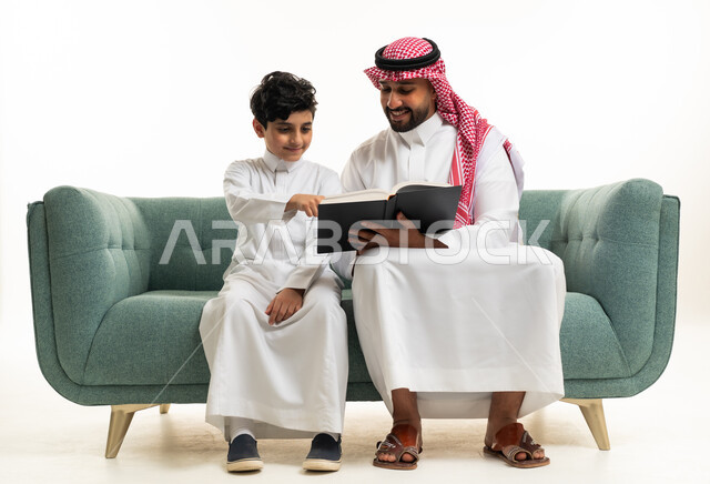 أب سعودي وابنه يقرآن كتاباً على أريكة خضراء بالداخل