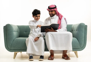 Saudi Father and Son Reading Book on Green Sofa Indoor