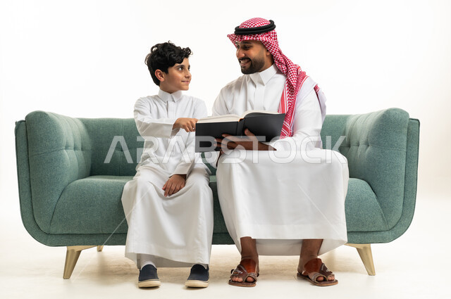 رجل وطفل سعودي يقرأان كتاباً على أريكة خضراء