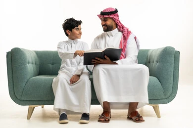 Saudi Father and Son Reading Book on Green Sofa