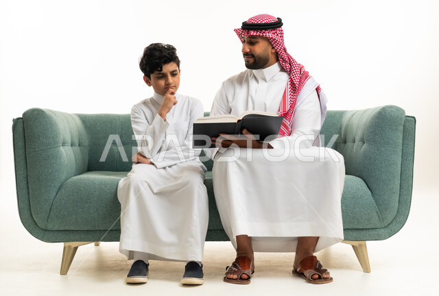 أب سعودي وابنه يقرآن كتاباً على الأريكة